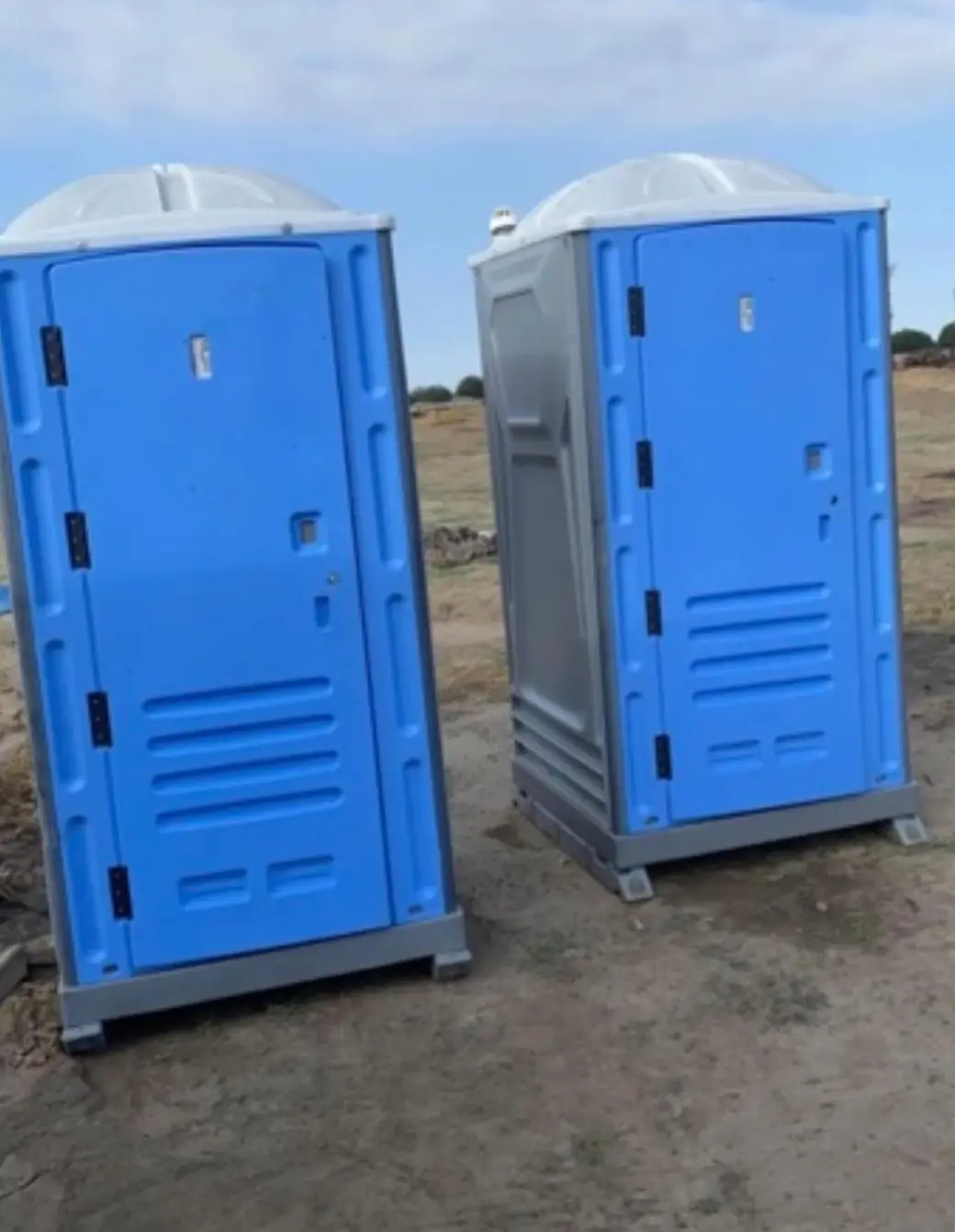 Pair of blue portable toilets standing on graded dirt at a building site