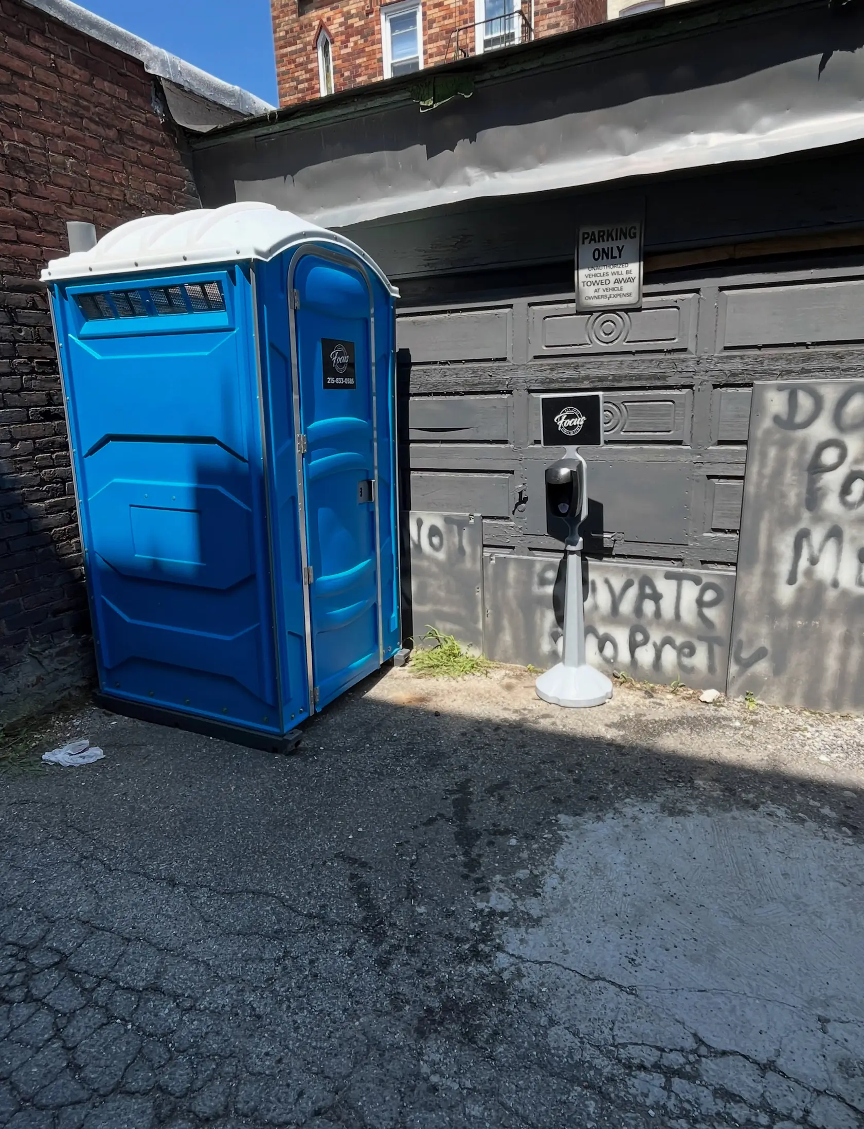 Blue portable toilet set in a narrow paved alley behind a brick building