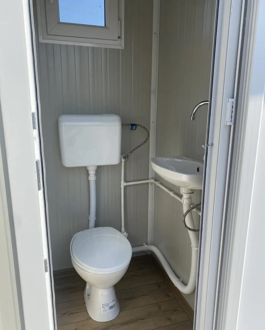 White portable restroom cabin interior with a flushing toilet and a small corner sink