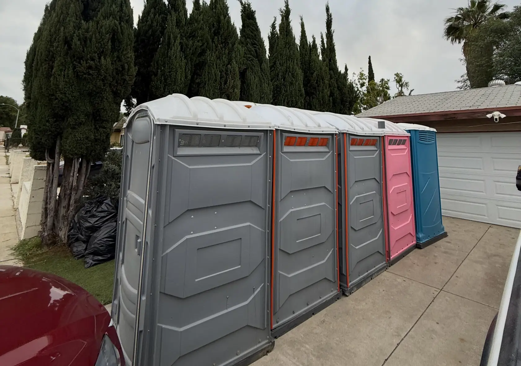 Gray, pink and blue portable toilets placed in a row along a residential driveway