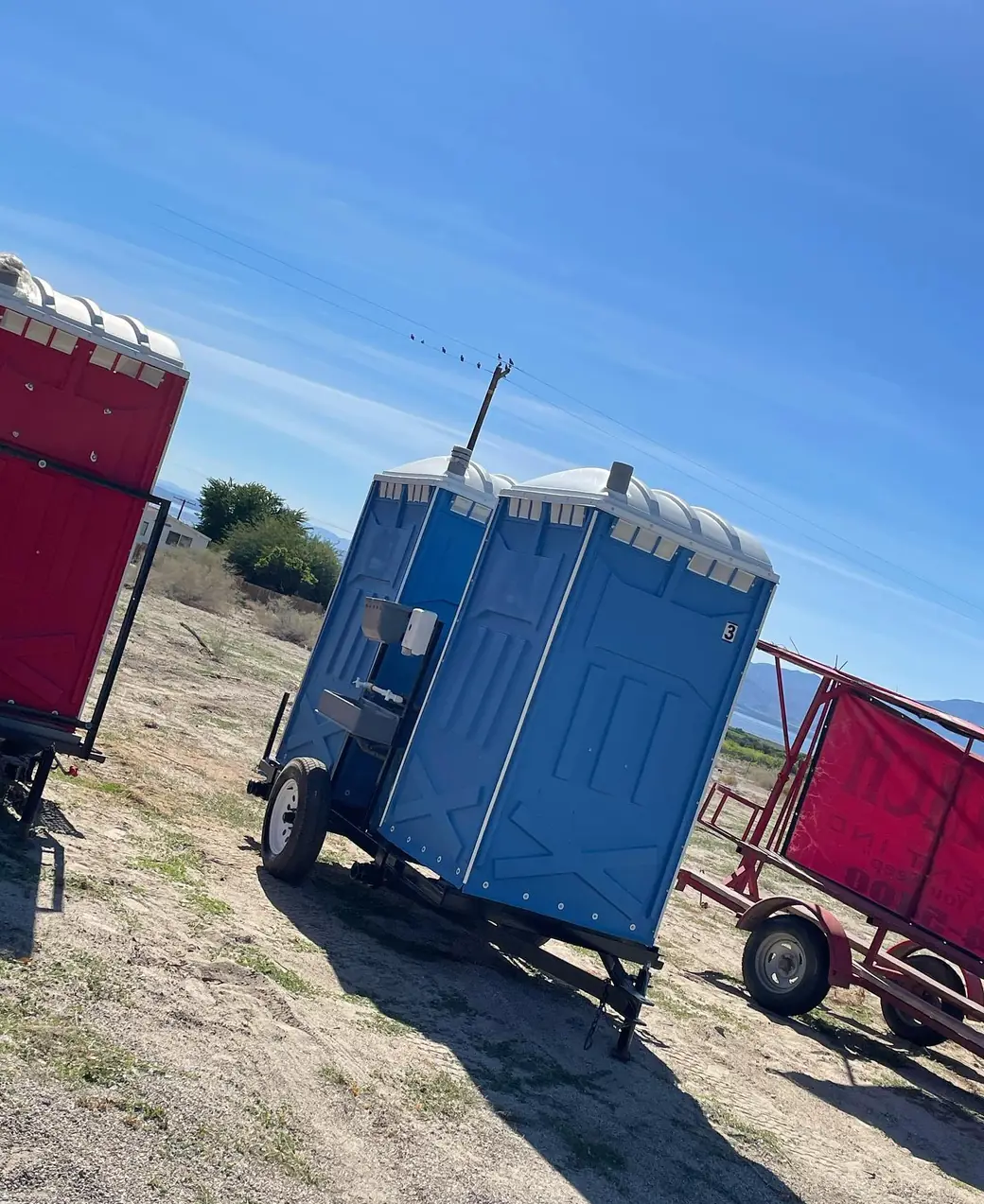 Two towable portable toilet trailers parked in an open dirt field