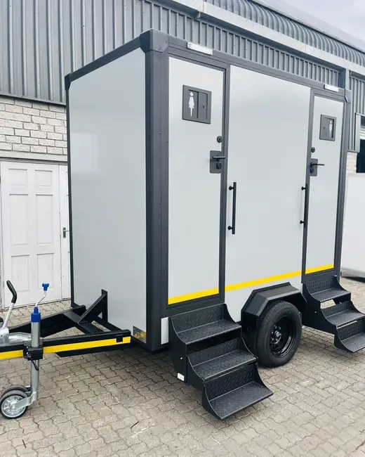 Two-stall restroom trailer with fold-down steps parked on pavers